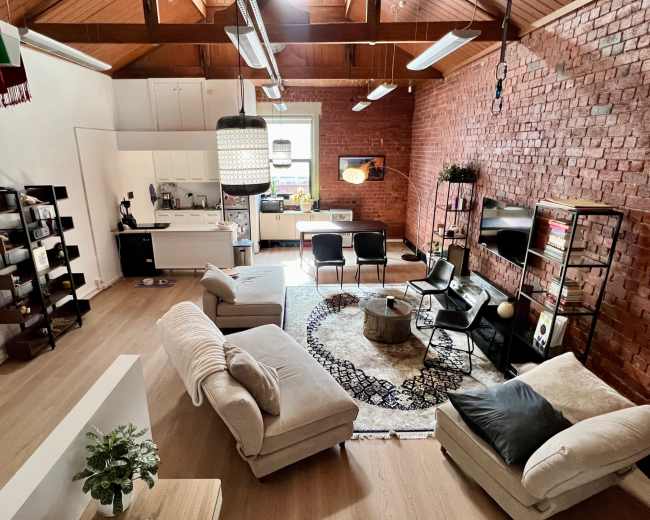 The image shows a modern living space featuring a cozy arrangement of furniture, including a large sectional sofa, a round coffee table, and a dining area with a kitchen in the background.