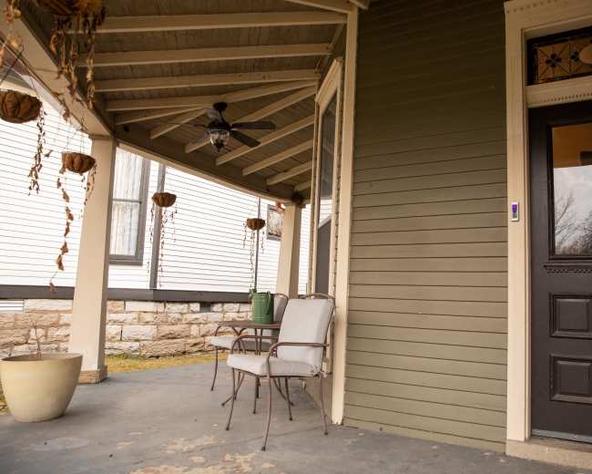 A porch features two chairs and a table near a door, with hanging planters above.