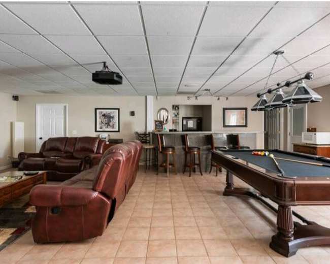 A spacious recreational room featuring a pool table, a seating area with leather couches, and a bar counter with high stools.
