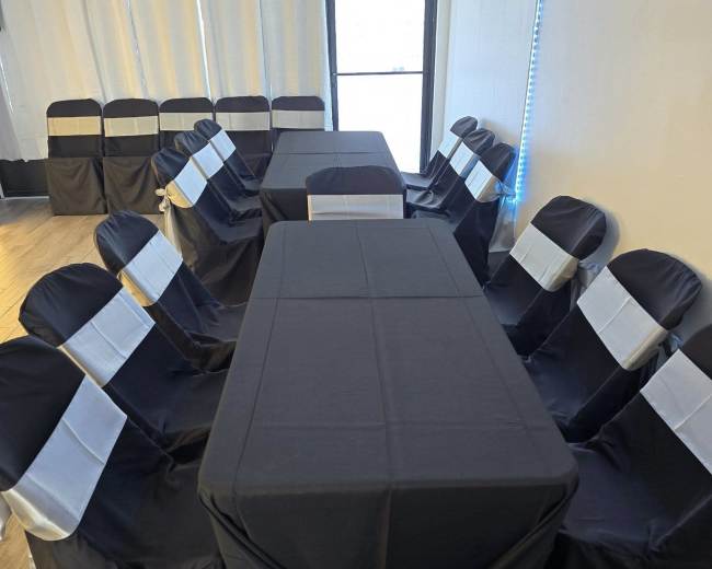 A dining area featuring several tables covered in black tablecloths with matching chairs adorned with silver sashes.