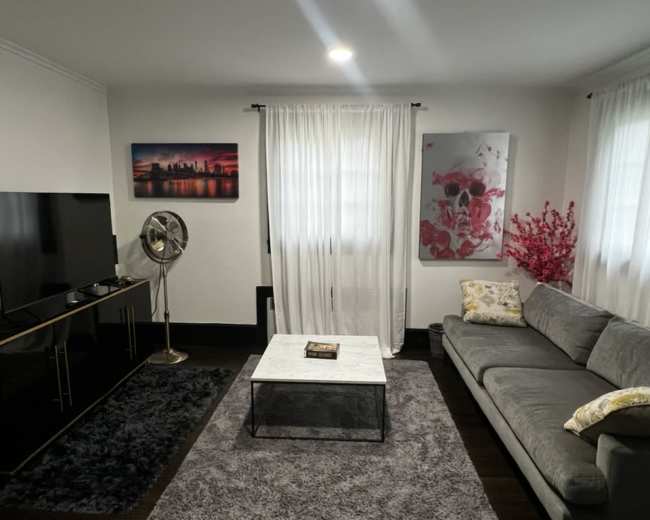 The image shows a modern living room with a gray sectional sofa, a marble coffee table, a large TV on a black console, and decorative wall art.