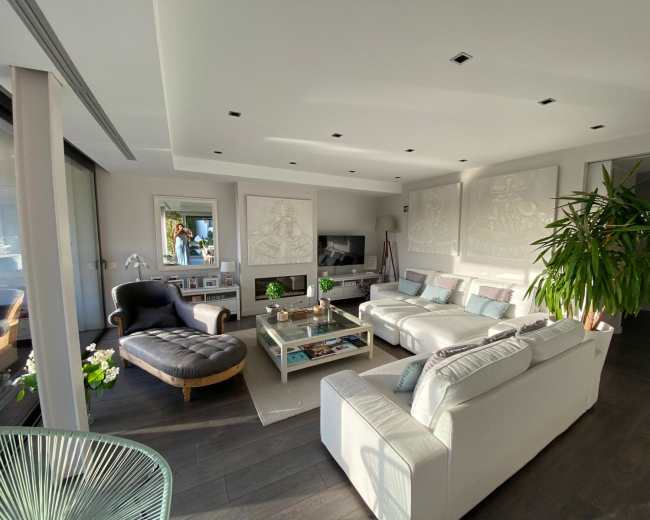 The image shows a bright, modern living room with a large sectional sofa, a coffee table, and decorative wall art.
