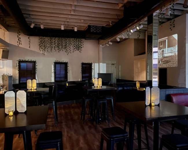 The image shows a dimly lit restaurant interior with tall tables, black seating, and a projection on the wall.