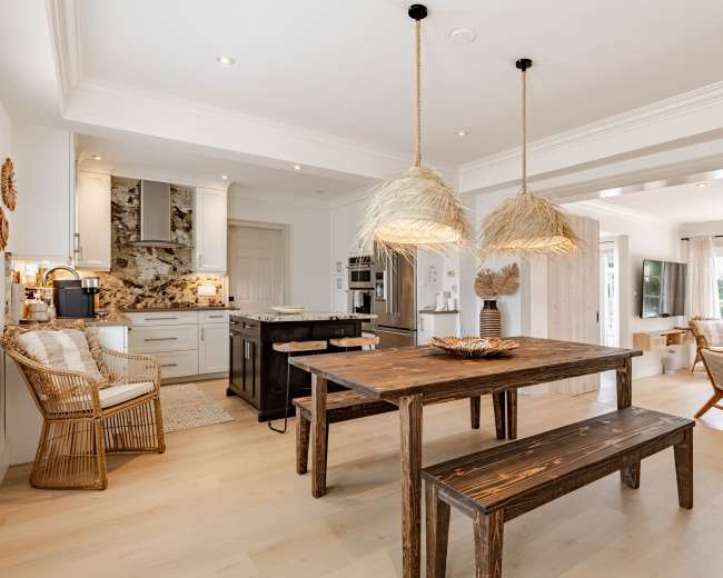 The image shows a modern kitchen and dining area with a wooden table, straw pendant lights, and a mix of seating options, including woven chairs and a sofa.