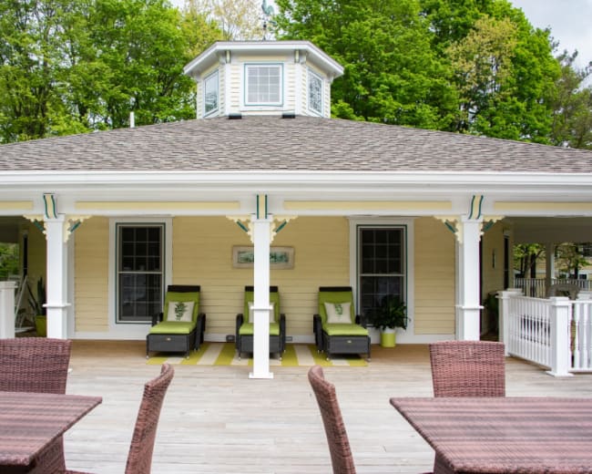The image shows a large, light-colored gazebo with a cupola, featuring green accents and outdoor seating arranged on a wooden deck.