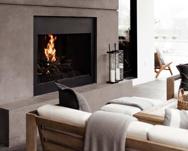 A modern living space with a concrete wall featuring a television above a fireplace, complemented by a wooden sofa with cushions and a coffee table.