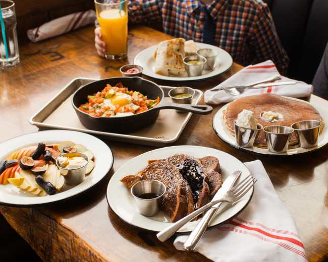 The table displays a variety of breakfast dishes, including French toast, a vegetable hash with an egg, and fruit sides, along with two glasses of orange juice.