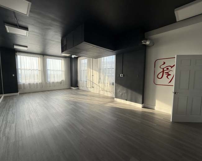 The image shows an empty room with large windows, gray walls, and a white door featuring a red design on one wall.