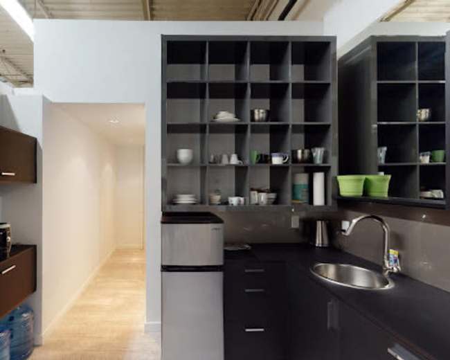 A modern kitchen layout with black cabinetry, a stainless steel sink, and a hallway leading to a well-lit area.