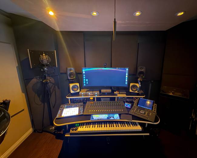 The image shows a modern music production studio setup with a computer, audio equipment, speakers, and a MIDI keyboard arranged on a desk.