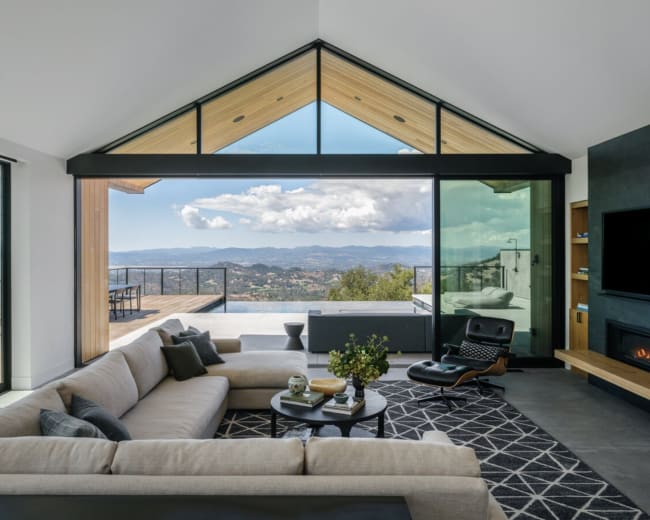 A modern living room with a large sectional sofa, a coffee table, and expansive windows offering a view of a mountainous landscape.