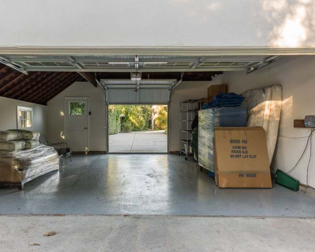 The image shows a garage with an open door, revealing stacks of items including mattresses, boxes, and paint cans inside.