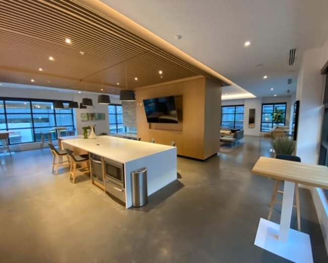 The image shows a modern open-plan kitchen and lounge area with sleek furniture and large windows.