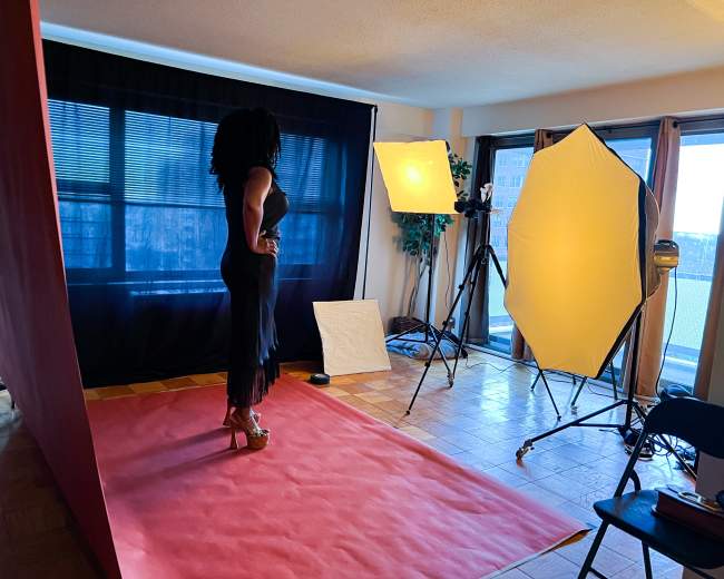 A woman poses on a red carpet in a studio set up with bright lighting and a black backdrop.