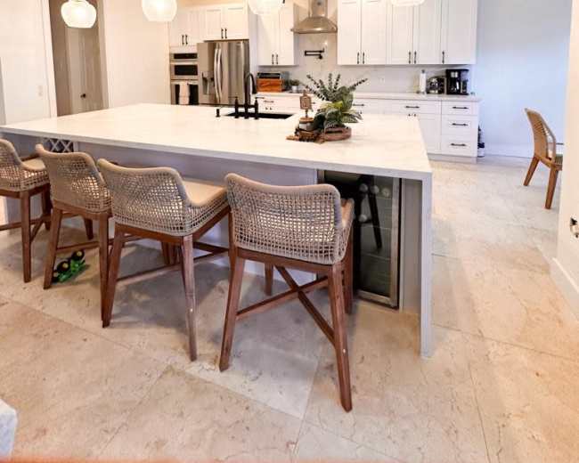The image shows a modern kitchen with a large island featuring bar seating, pendant lights, and stainless steel appliances.