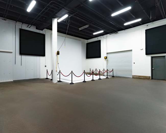 The image shows a large, empty indoor space with a smooth floor, white walls, and two large screens mounted on the walls.