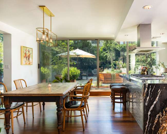 A modern kitchen with a dining table and a view of a patio featuring greenery and an outdoor umbrella.
