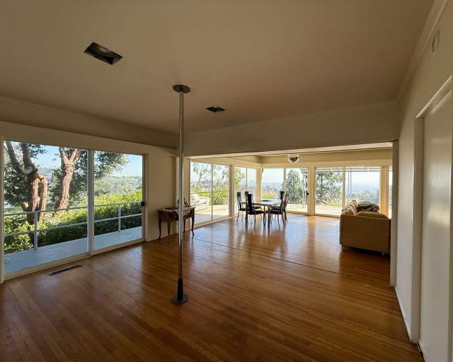 A spacious living area features large windows that offer a view of greenery and a distant landscape.