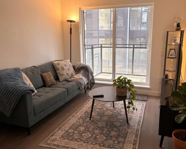 The image shows a modern living room with a teal sofa, a round coffee table, and large windows providing natural light.