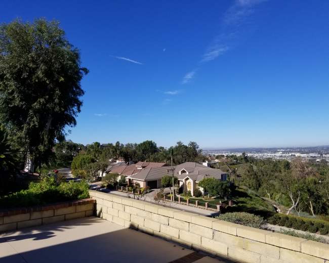 The image shows a scenic view of suburban homes on a hillside under a clear blue sky.