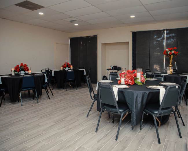 A banquet room with several round tables set with black tablecloths, plates, and floral centerpieces.