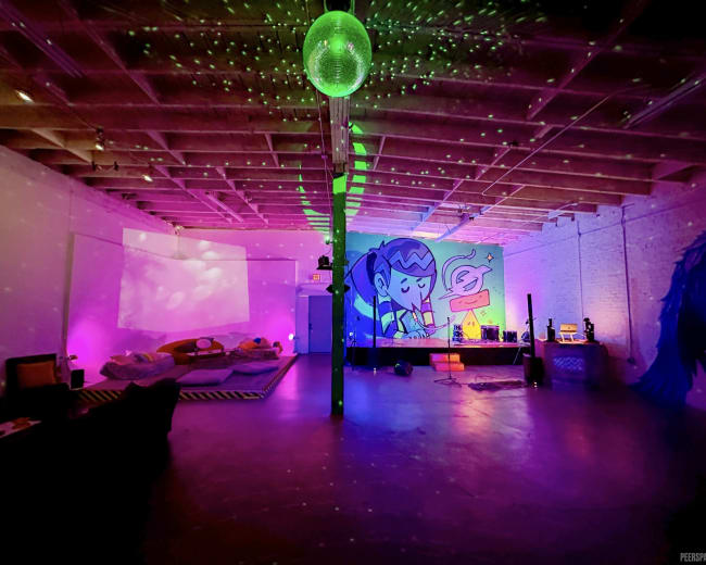 The image shows a colorful indoor space with a disco ball, vibrant lighting, and a mural on the wall, featuring a cartoon character.