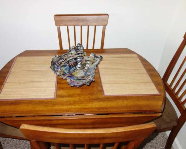 A wooden dining table with bamboo placemats is set with a decorative glass bowl in the center, surrounded by four wooden chairs.
