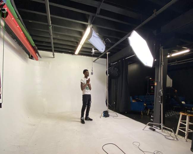 A person stands in a photography studio with a white backdrop and lighting equipment.