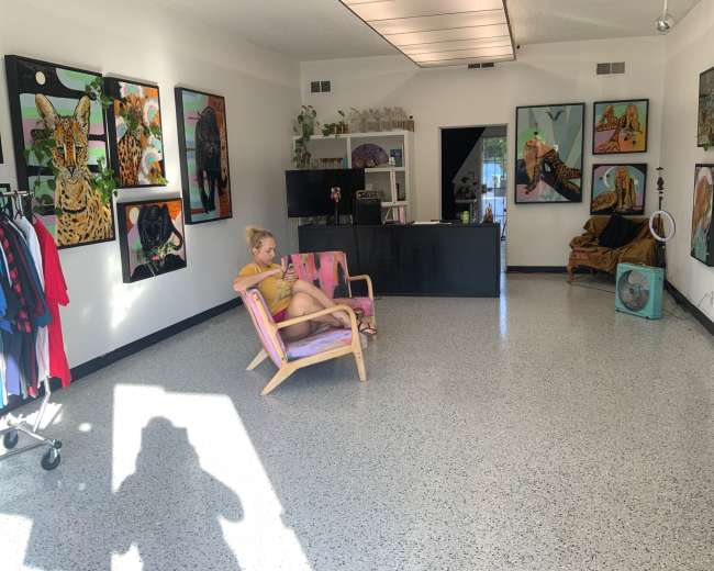A woman sits on a wooden chair in a gallery-like room decorated with animal-themed artwork and clothing racks.