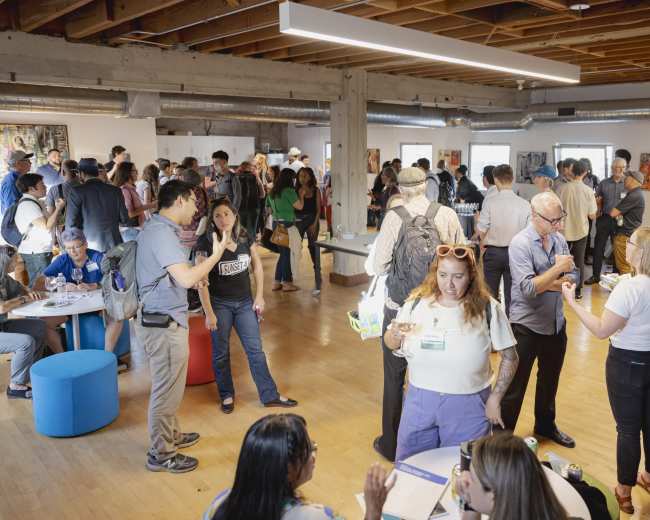 A group of people is gathered in a spacious, well-lit room with modern decor, engaging in conversation and networking.