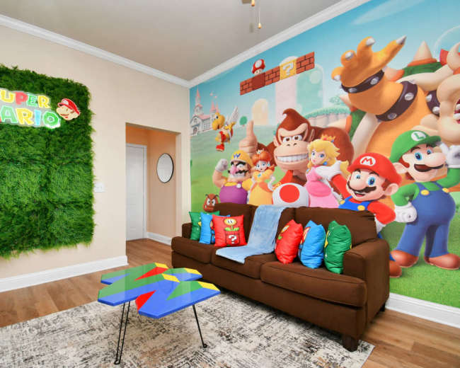 The room features a brown sofa with colorful cushions and a vibrant Super Mario-themed mural on one wall, accompanied by a green, leafy decor piece.