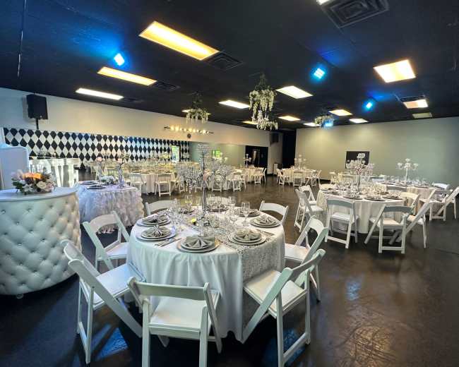 A banquet hall set up for an event, featuring multiple round tables with white tablecloths, elegant place settings, and decorative centerpieces.