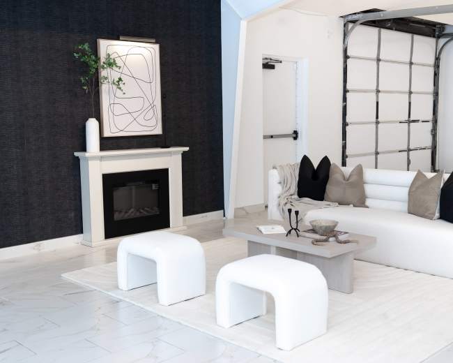 The image shows a modern living room with a white sofa, a coffee table, and a fireplace surrounded by dark wallpaper and light-colored flooring.