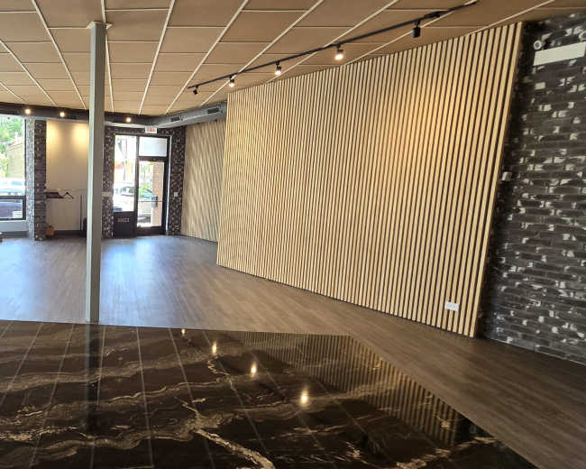 An empty commercial space with large windows, wooden paneling, and a polished black and white marble floor.