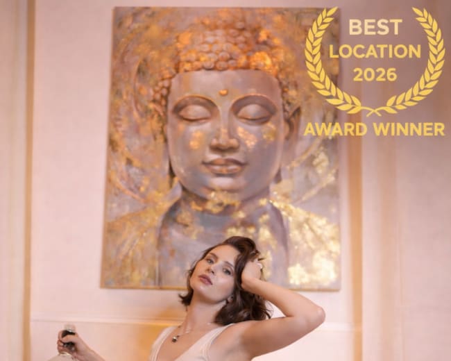 A woman poses with a bottle of whiskey in a stylish room featuring a large Buddha wall art.