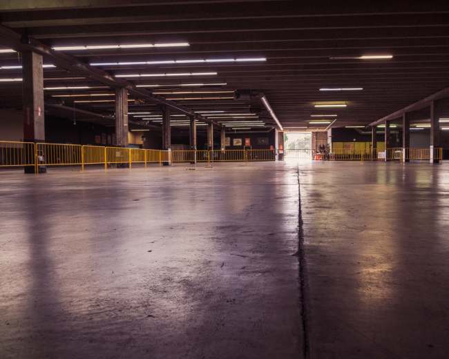 The image shows an empty, well-lit parking garage with a smooth concrete floor and barriers along the sides.