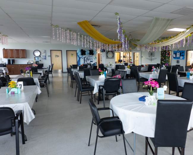 The dining area features multiple tables with white tablecloths, decorated with flowers, and colorful streamers hanging from the ceiling.