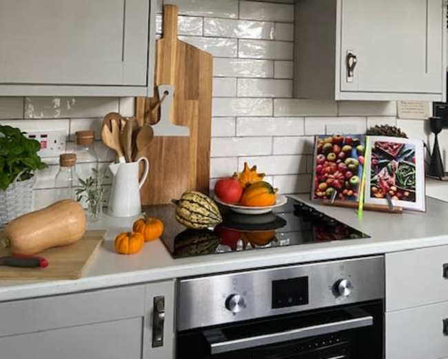 A modern kitchen features gray cabinets, a stainless steel hood above a stove, and a countertop adorned with various fruits, vegetables, and cooking utensils.