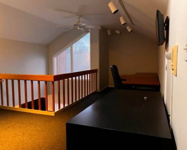 A lofted space featuring a desk, a chair, a television, and a railing overlooking a lower level.