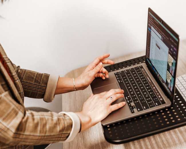 A person is typing on a laptop while seated at a desk with a wooden surface.