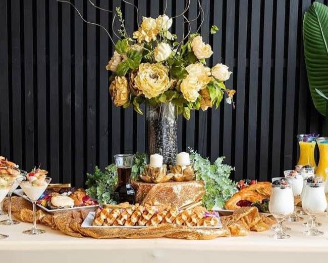 A beautifully arranged buffet table features a floral centerpiece, an assortment of desserts, baked goods, and beverages.