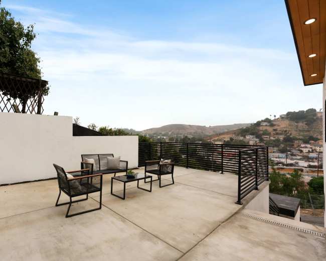 The image shows a spacious outdoor terrace with metal furniture and a view of a hilly landscape.