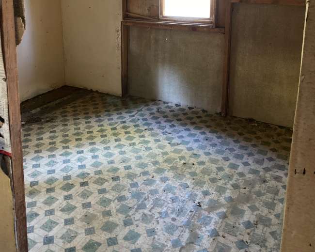 The image shows a vacant room with a window, bare walls, and a patterned floor.