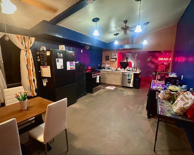 A spacious kitchen and dining area features a black refrigerator, a wooden table with white chairs, and various food items spread across counters.