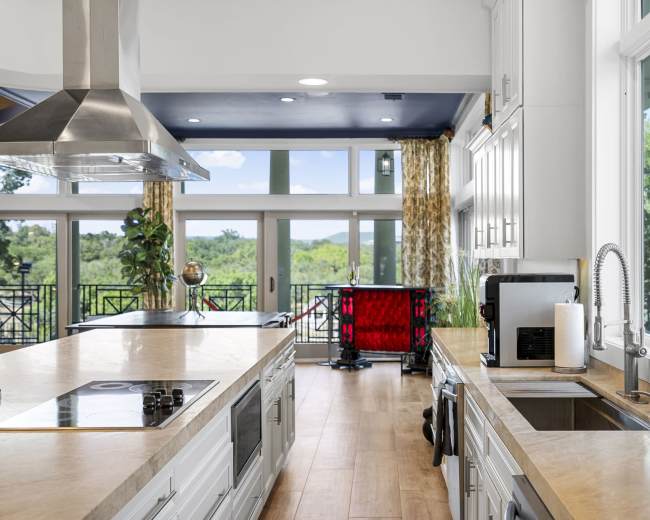 A bright kitchen features modern appliances, a large island, and expansive windows overlooking a green landscape.