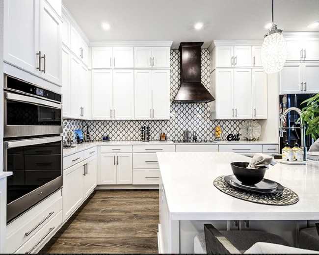 The kitchen features white cabinetry, a patterned backsplash, a stainless steel hood, and a central island with a black bowl on a decorative placemat.