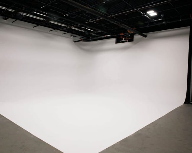 The image shows a large, curved white backdrop within a studio space.