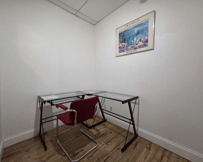 The image shows a small office space with two glass-top desks and a red chair against a white wall.