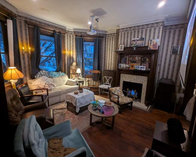 The room features a cozy living area with a mix of vintage furniture, including a sofa, armchairs, and a coffee table, all arranged around a fireplace.