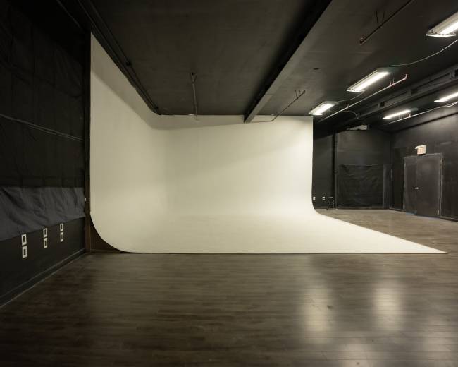 The image shows a photography studio featuring a large, curved white backdrop against a dark floor and walls.